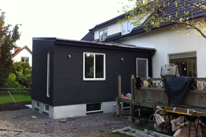 Tillbyggnad med källare och överliggande plan i liggande svartmålad Z-panel.